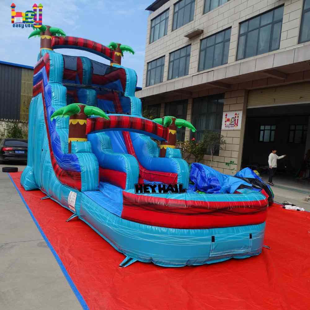 Opposite angle view of blue red single lane water slide with front pool and palm-tree accents
