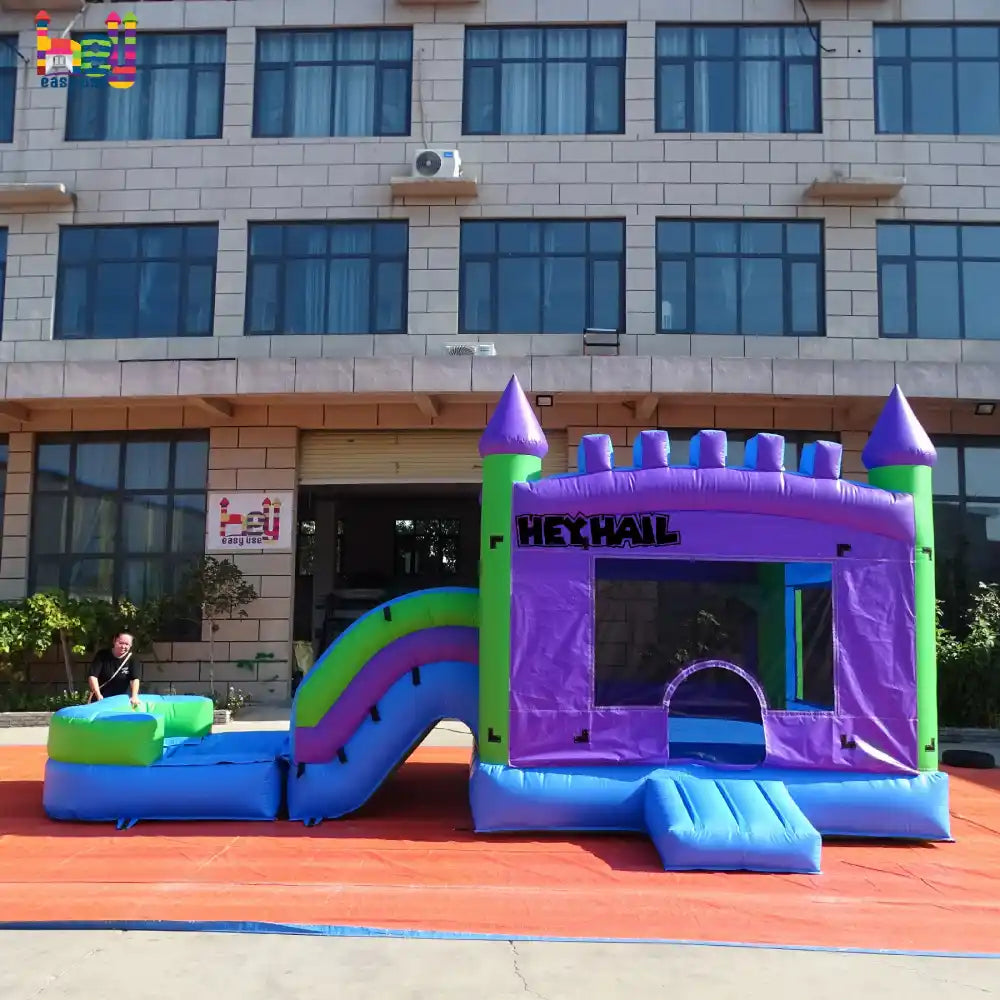 Outdoor front view of a purple, blue, and green single-lane inflatable castle combo with a slide