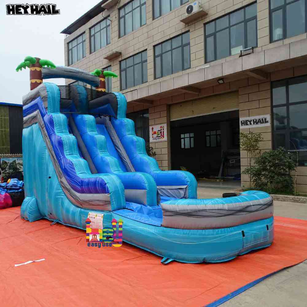Angled view of blue gray single lane water slide with front pool and palm-tree accents