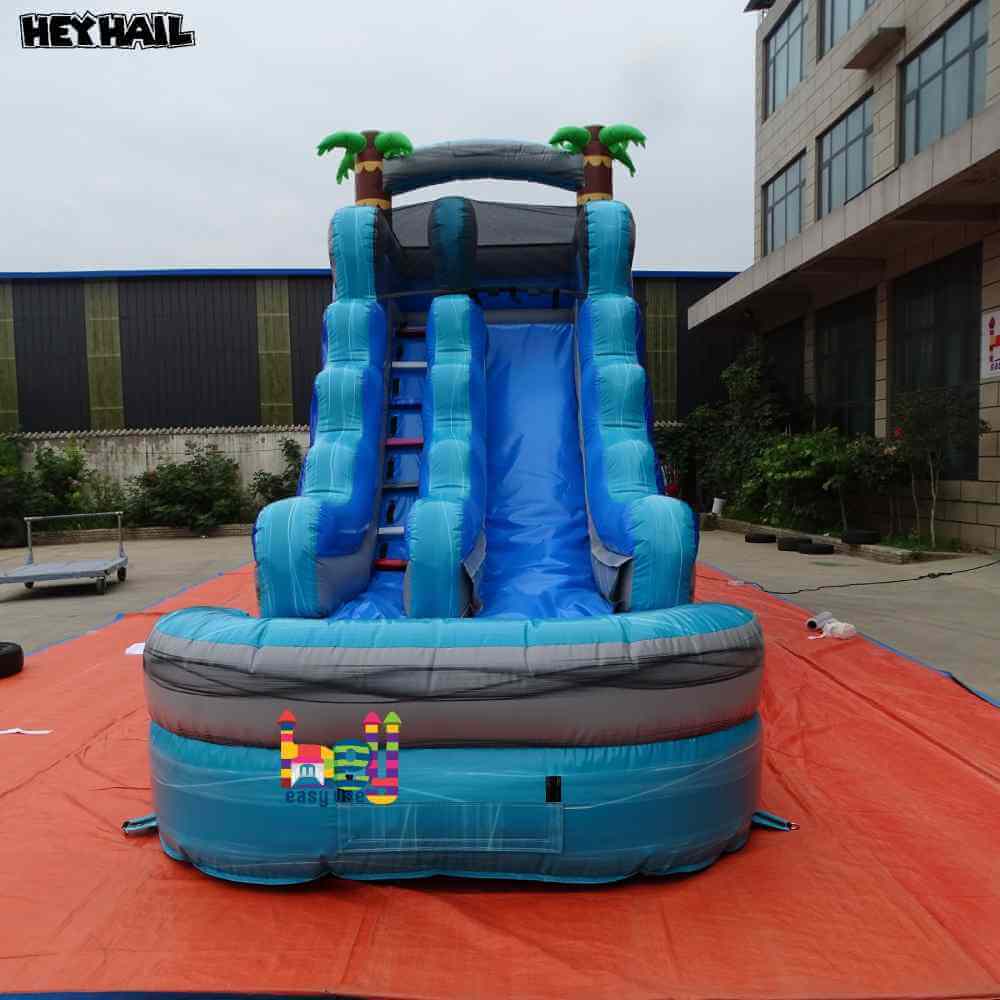 Front view of blue gray single lane water slide with front pool and palm-tree accents