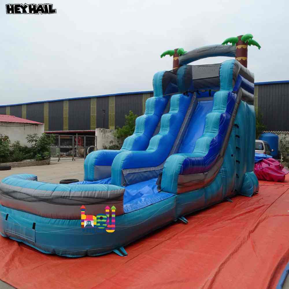 Opposite angle view of blue gray single lane water slide with front pool and palm-tree accents