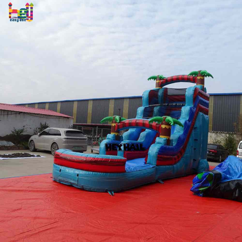 Angled view of blue red single lane water slide with front pool and palm-tree accents