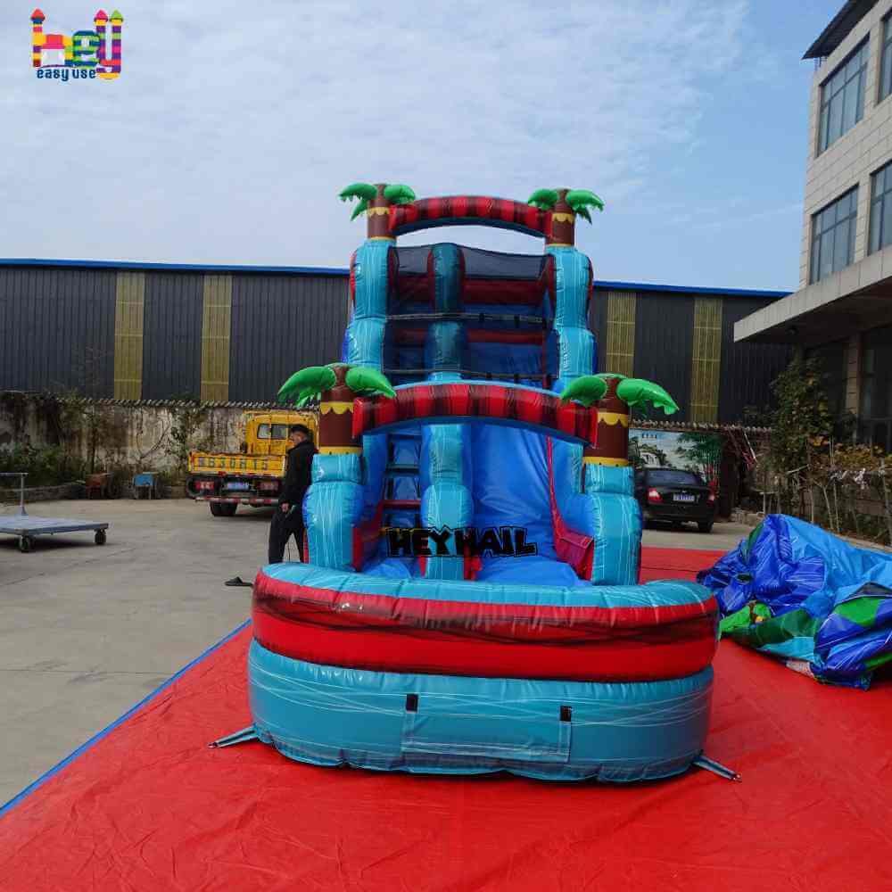 Front view of blue red single lane water slide with front pool and palm-tree accents