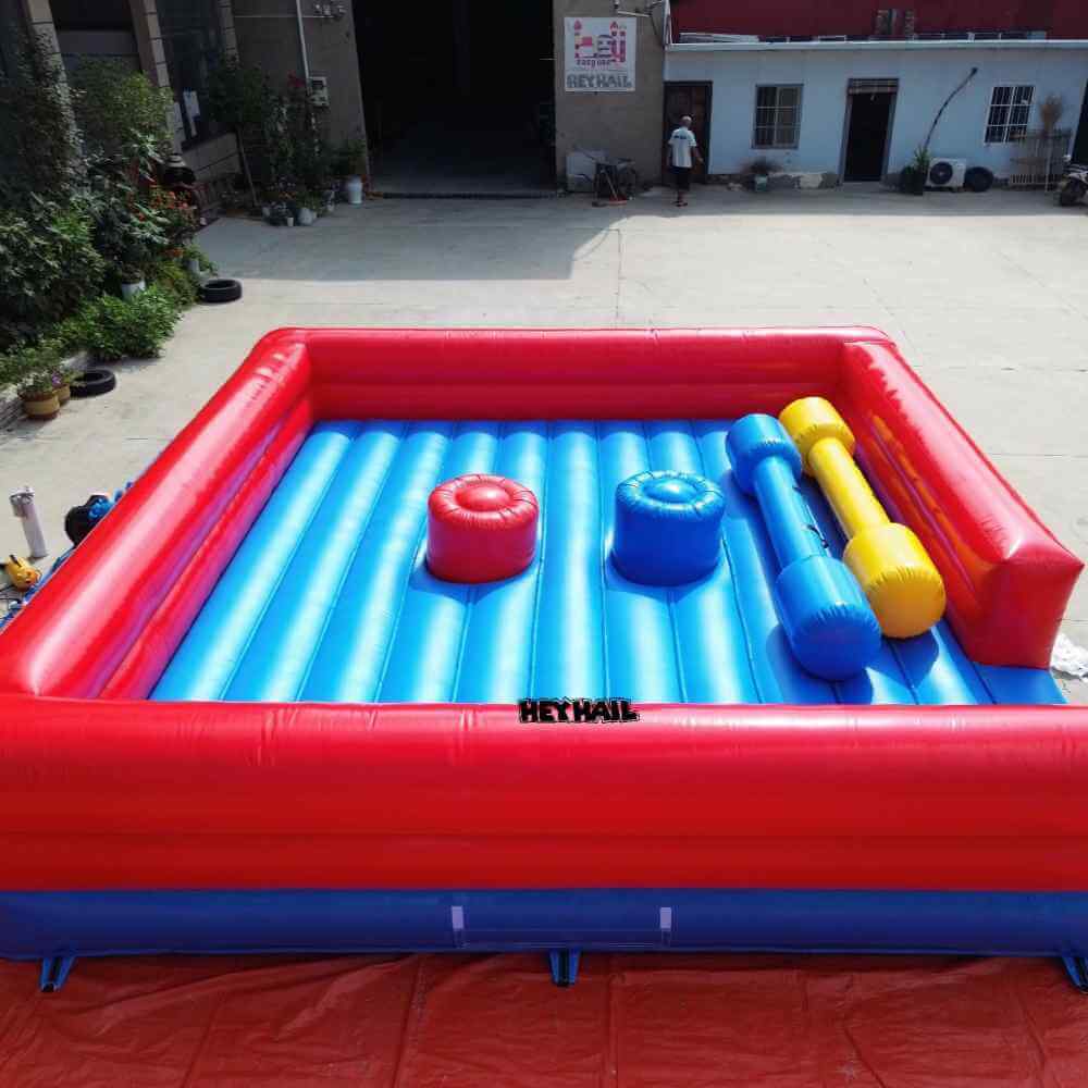 Red-and-blue inflatable jousting arena with two pedestals and blue and yellow poles