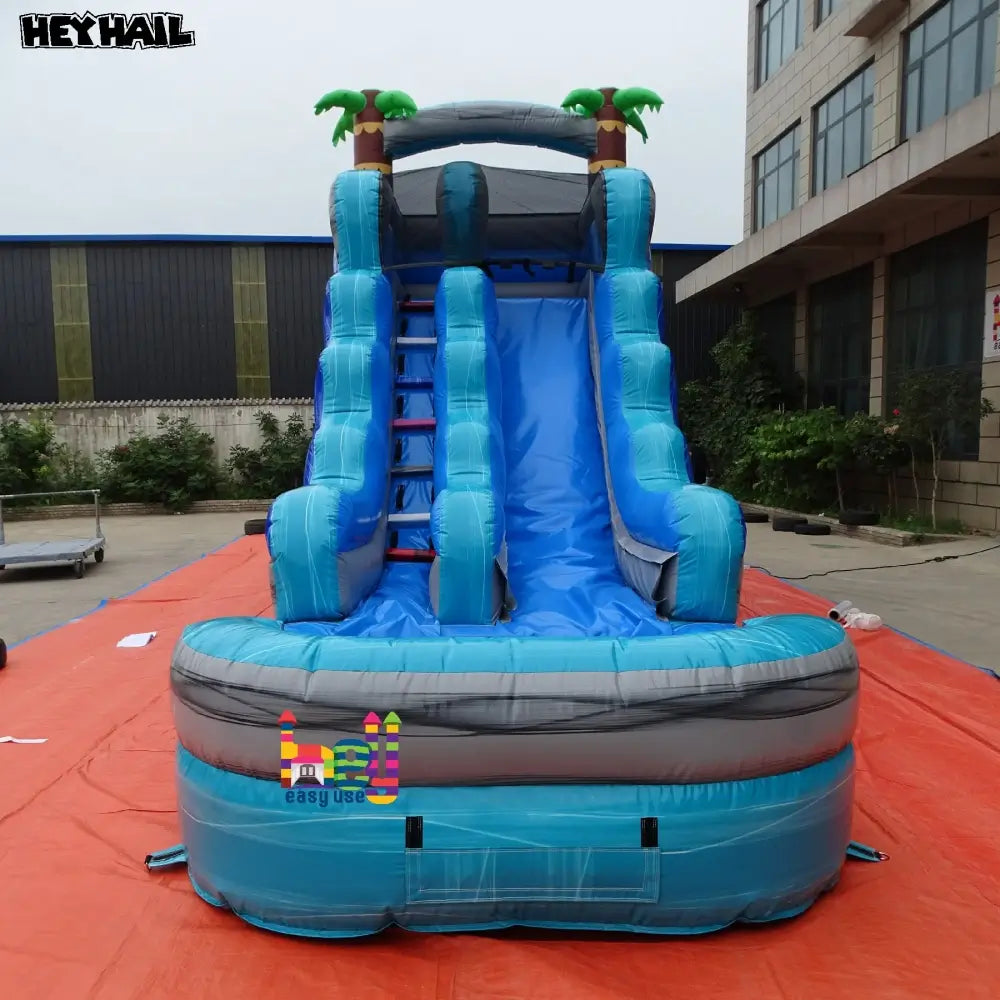 Outdoor front view of a marble-blue single-lane inflatable water slide with a gray landing pool and palm-tree arch
