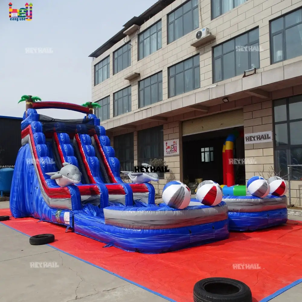 Outdoor close front view of a marble-blue dual-lane inflatable water slide with dolphin accents and beach balls