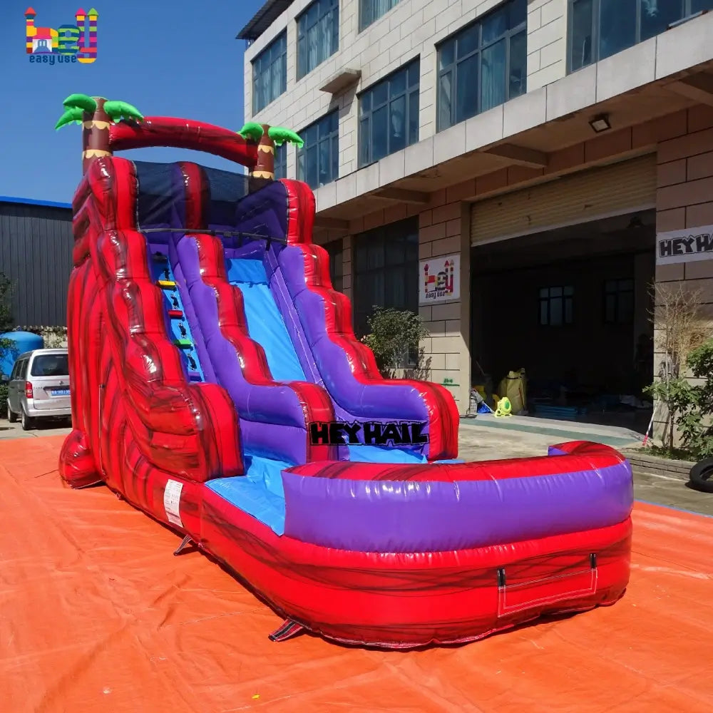 Outdoor front-left view of red-and-purple front-load water slide with blue slide lane, attached landing pool, and palm-tree accents