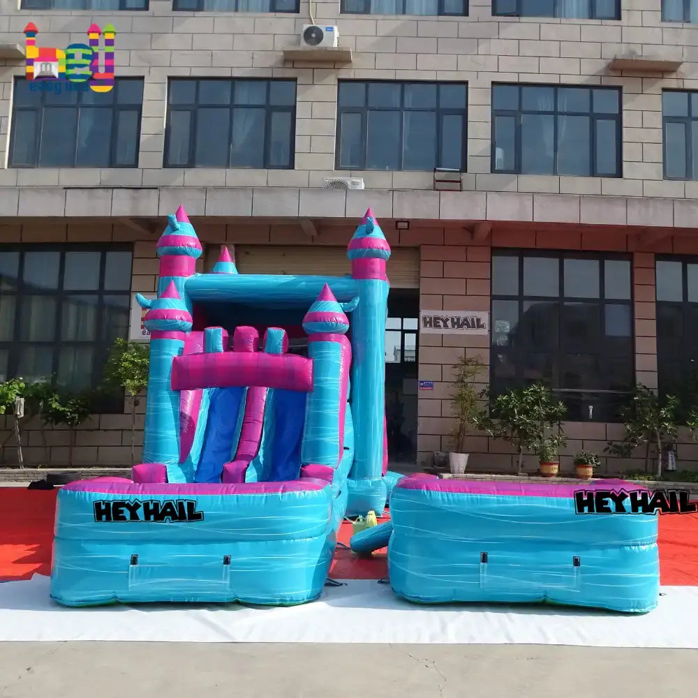Outdoor front view of a blue-and-pink inflatable castle combo with a slide and two rectangular landing pool sections