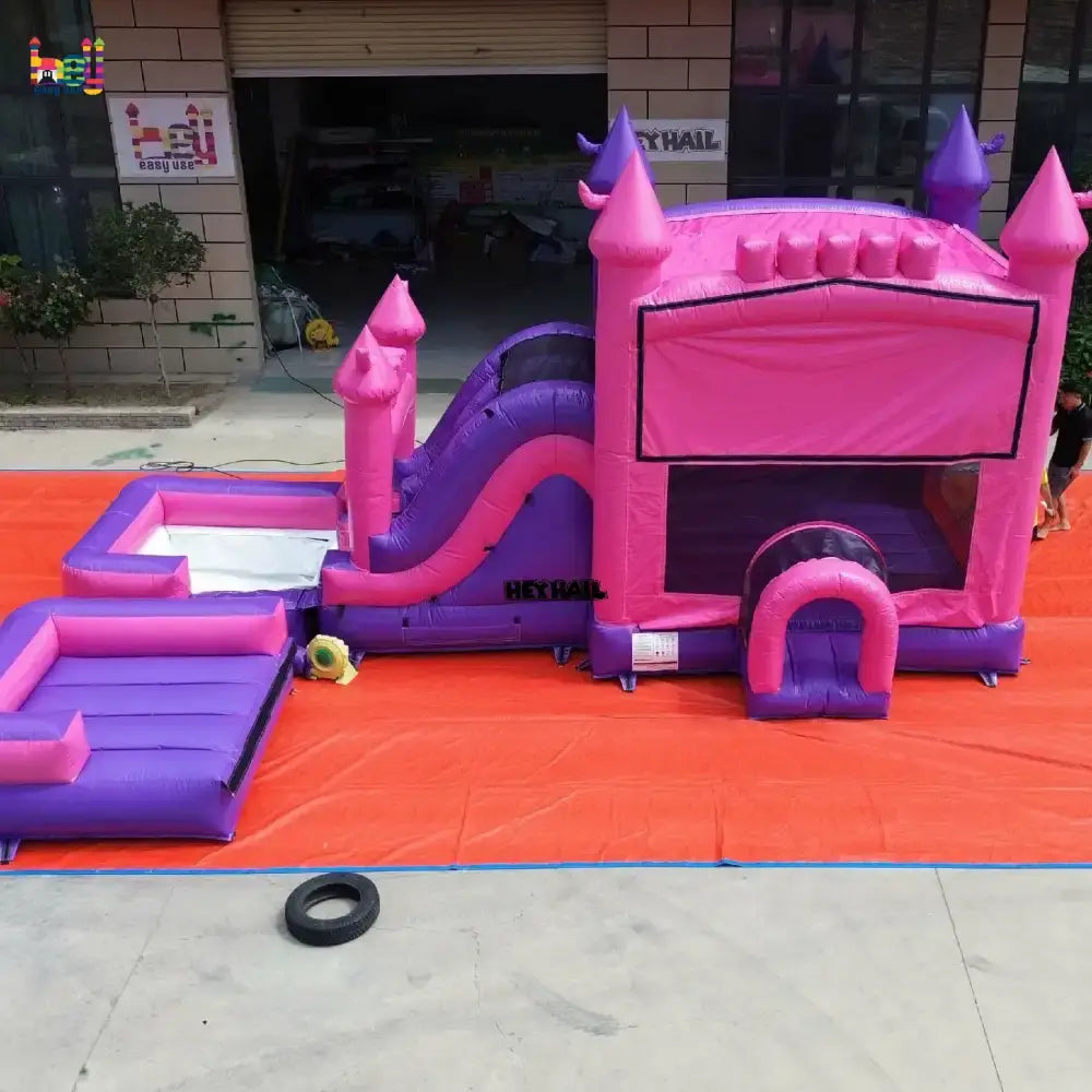 Outdoor side view of a pink and purple inflatable castle wet dry combo with a slide and two rectangular landing pools